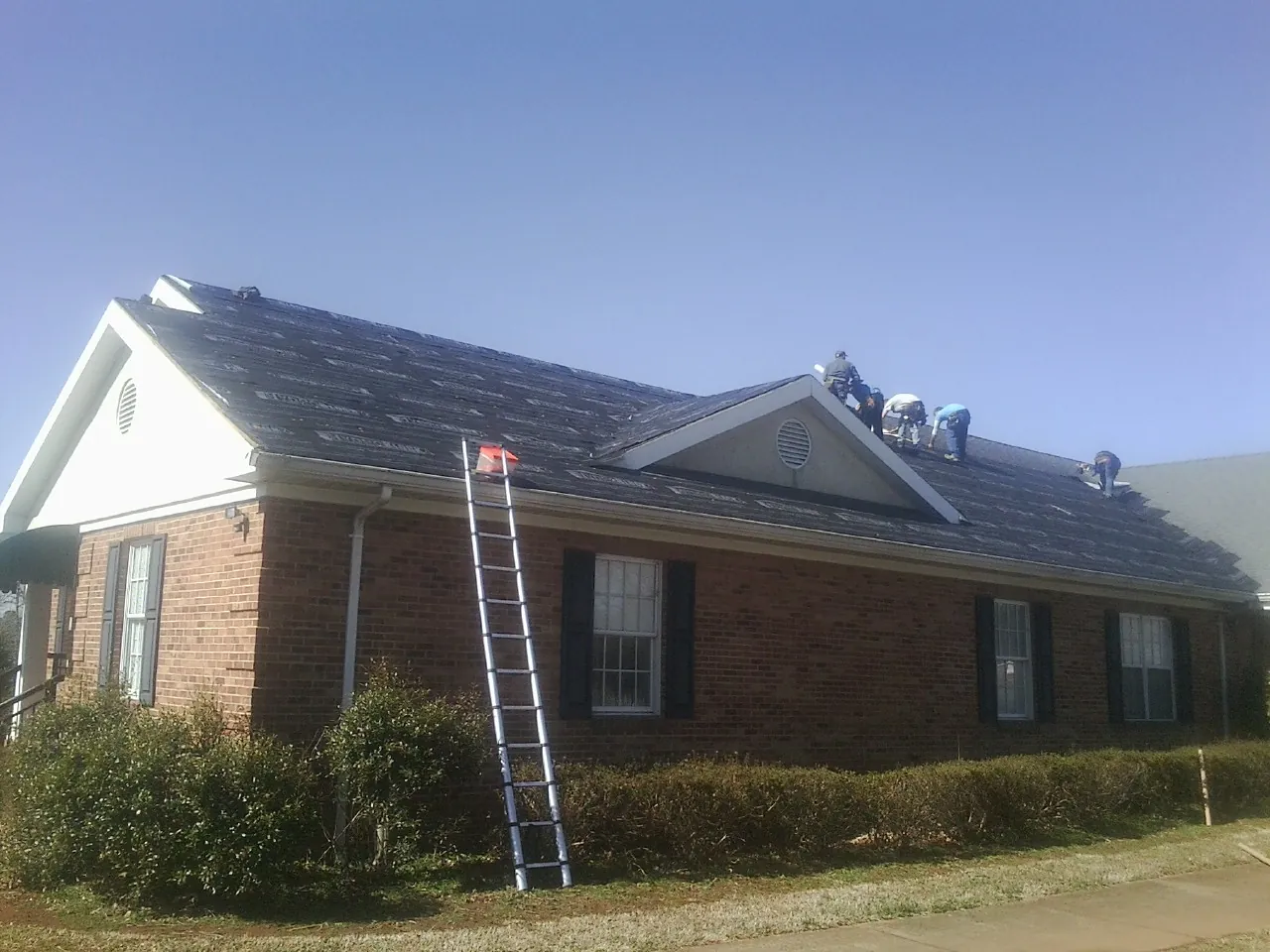 Crew tearing shingles off a brick ranch roof with a ladder set — Emergency Roof Repair work by our crew in Granite Bay