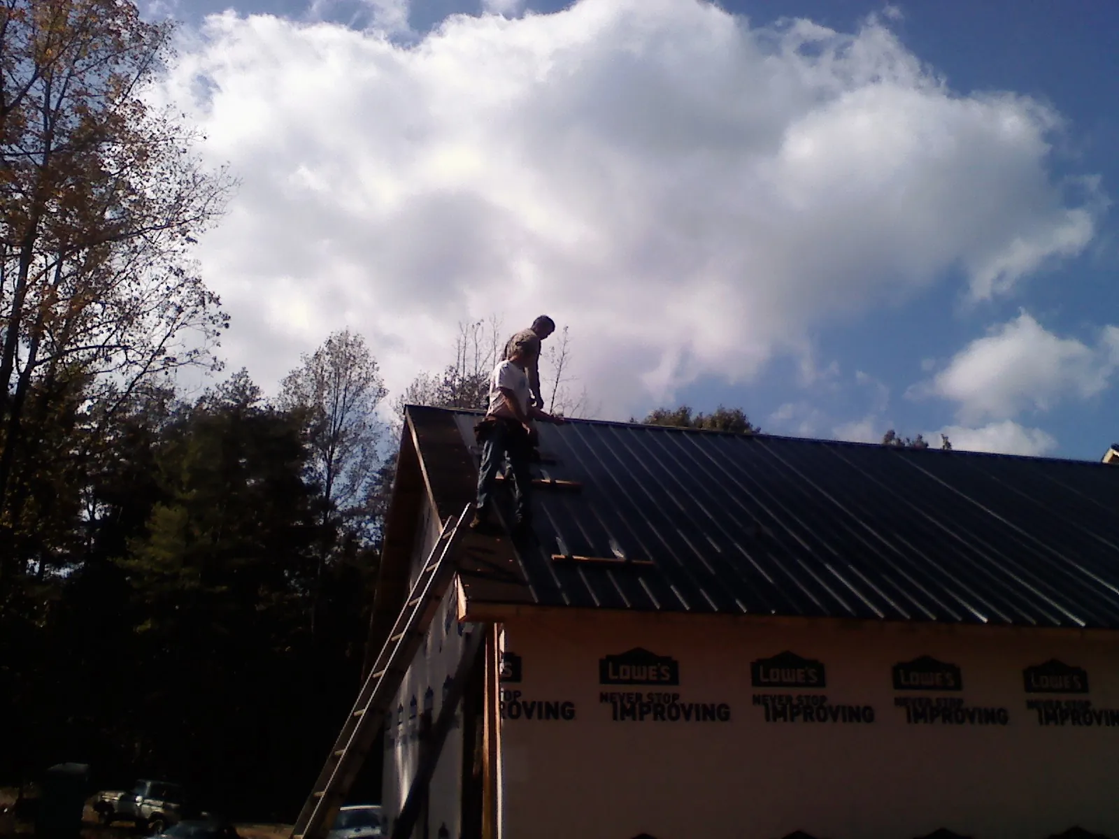 Roofer fastening dark metal panels high against a cloudy sky, from a Roof Inspection job in Granite Bay