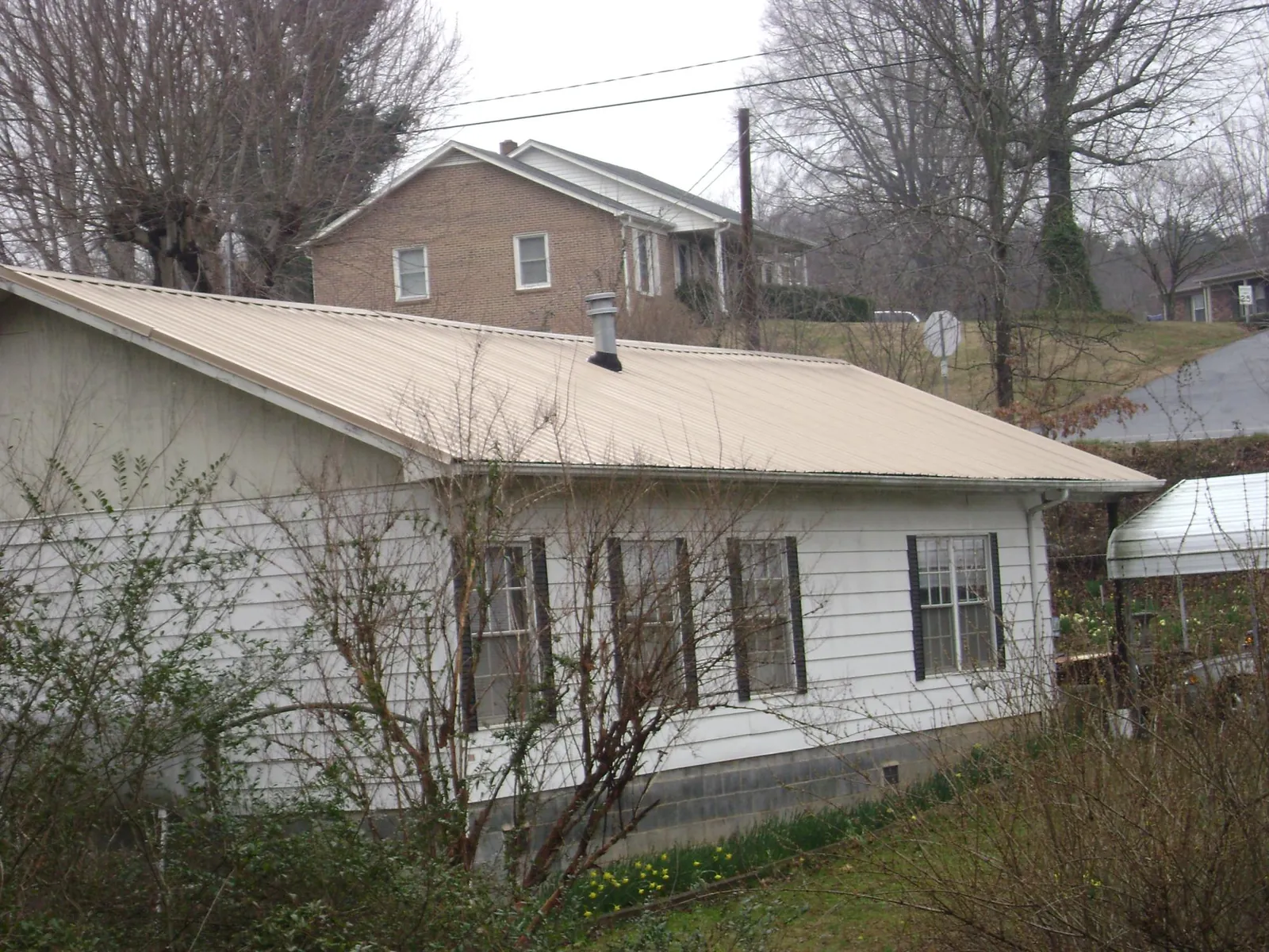 Tan metal roof on a white sided house set into a hillside — Commercial Roofing by Roofing Brothers in Granite Bay